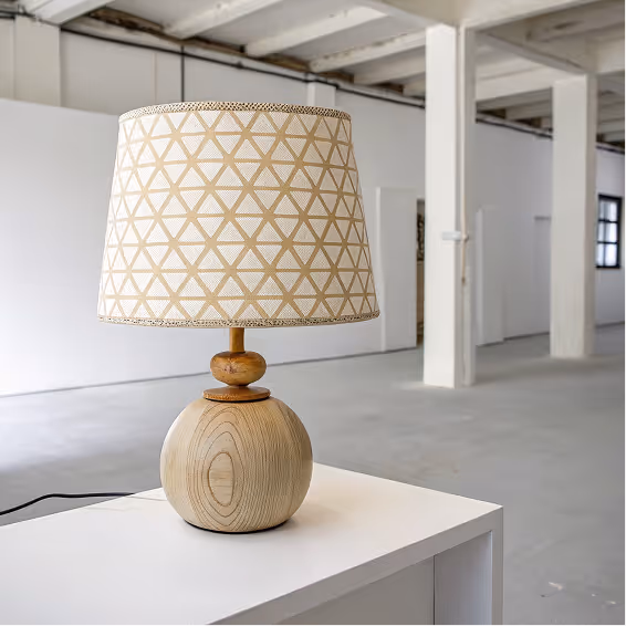 Wooden table lamp with a beige geometric patterned shade on a white surface in a spacious, industrial-style room.